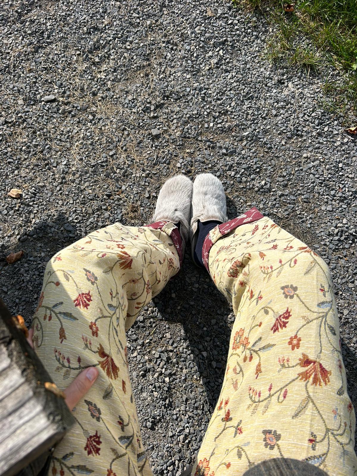 Person wearing floral pants and gray shoes on a gravel path