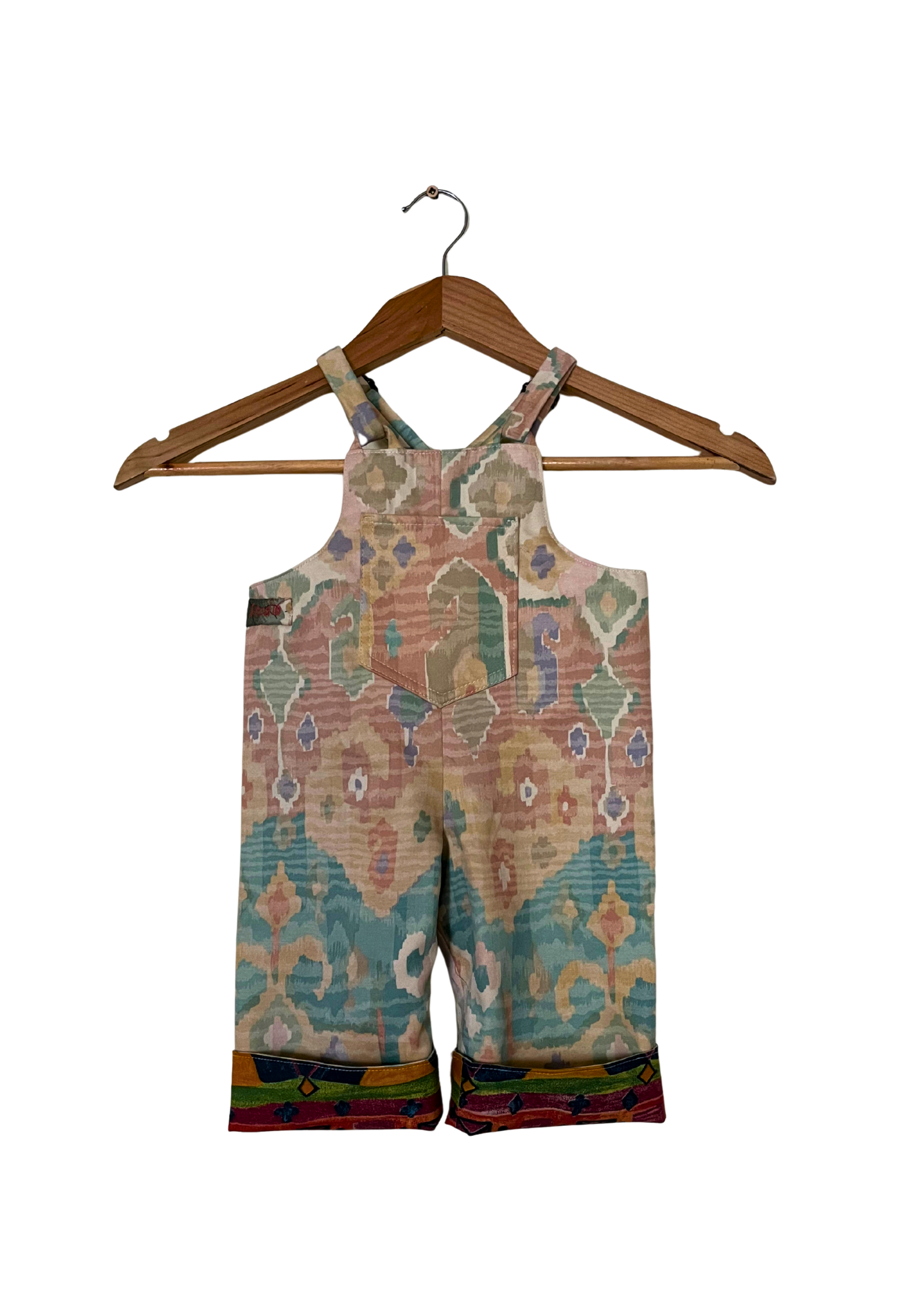 Colorful patterned overalls on a wooden hanger against a white background