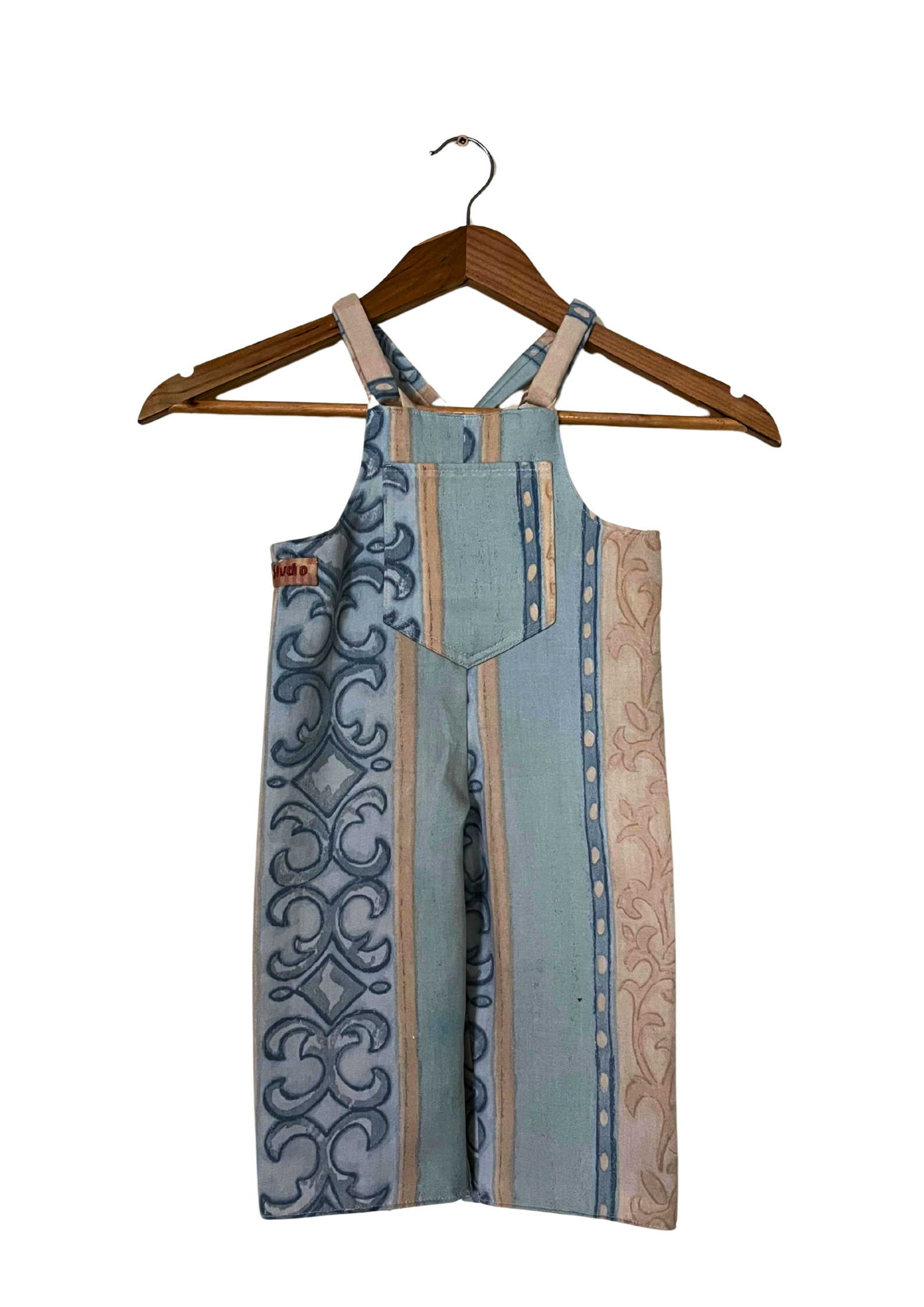 Patterned overalls on a wooden hanger against a white background