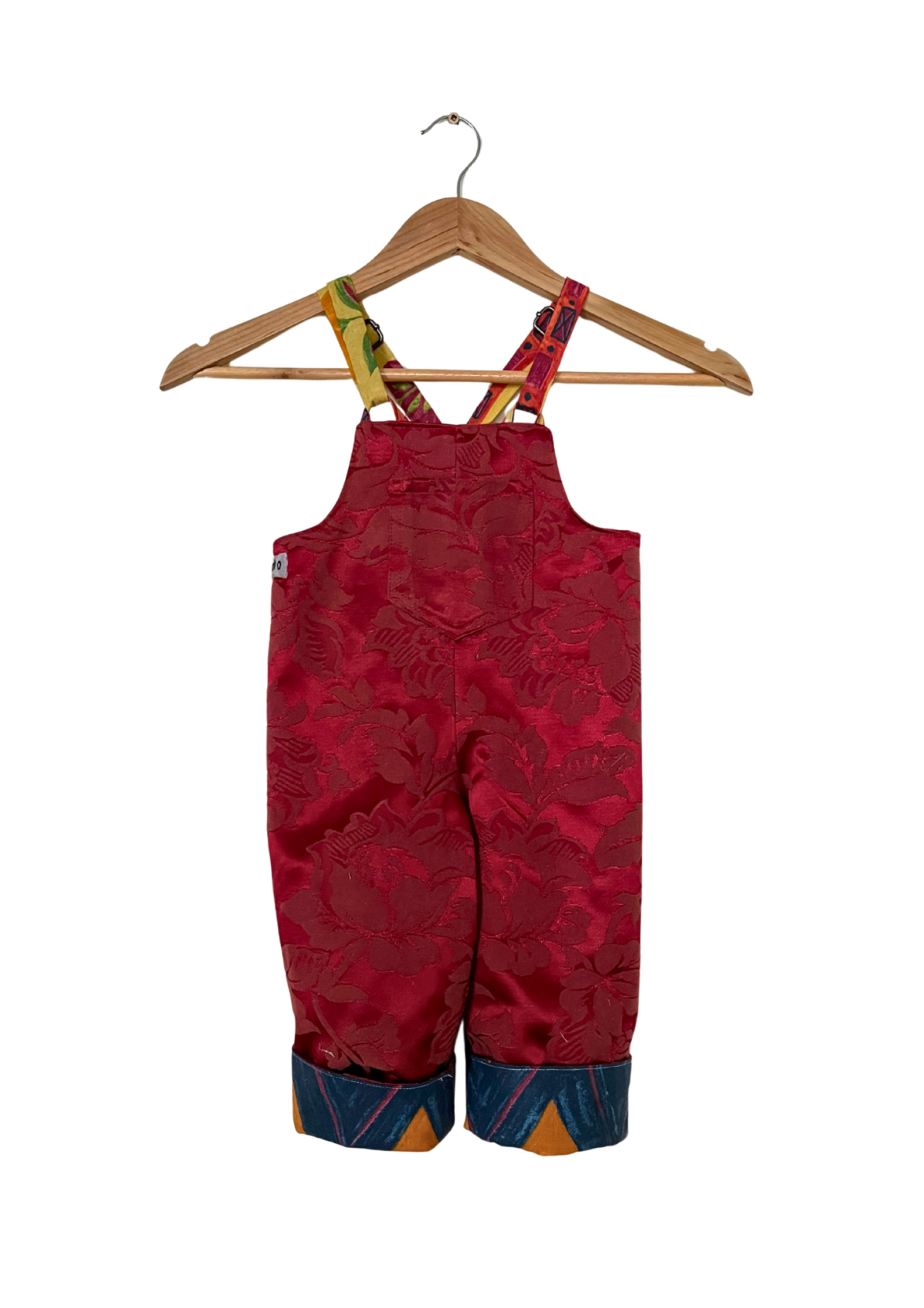 Red patterned overalls on a wooden hanger against a white background