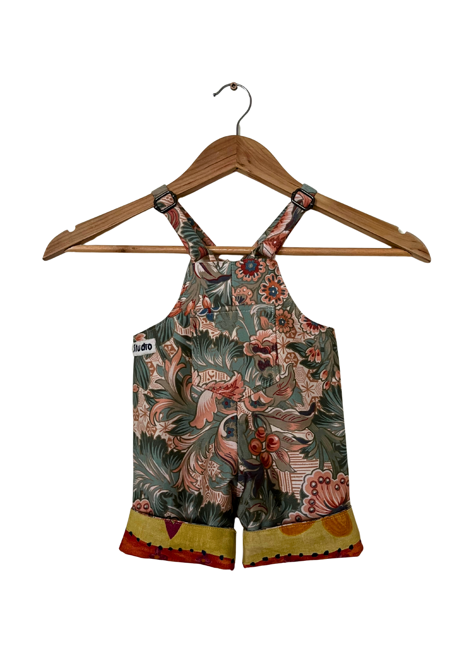 Floral-patterned overalls on a wooden hanger against a white background