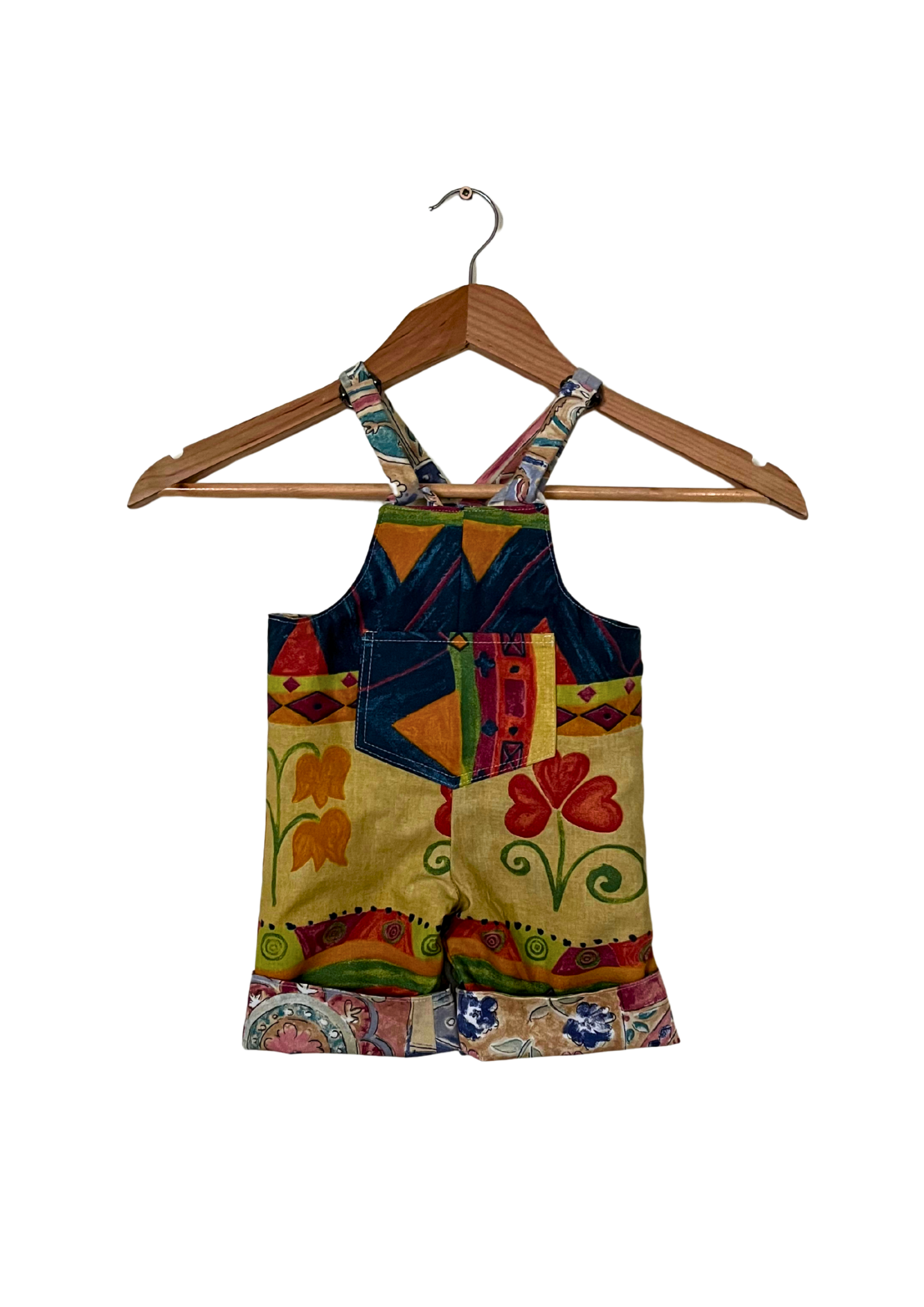 Colorful patchwork overalls on a wooden hanger against a white background