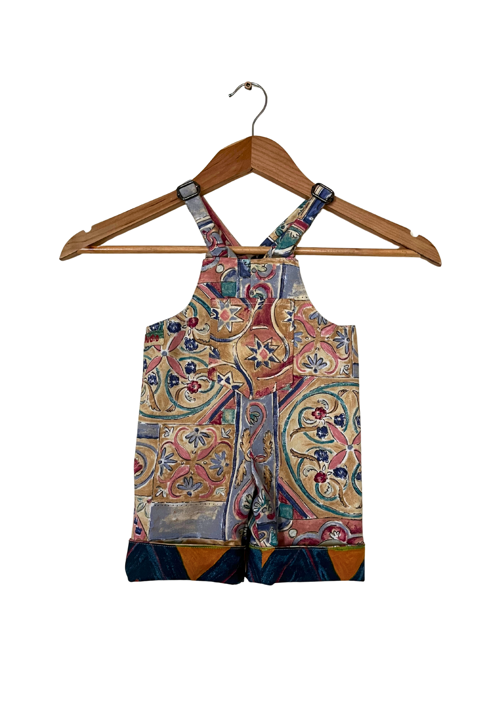 Colorful patterned overalls on a wooden hanger against a white background