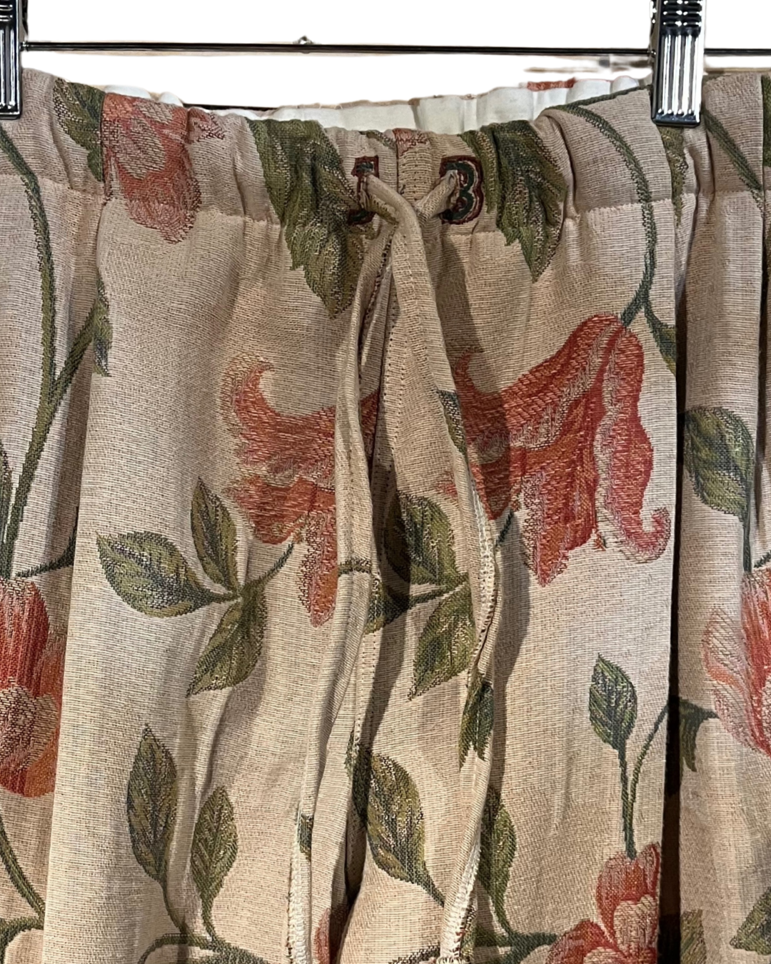 Floral patterned curtain with red flowers and green leaves on a beige background.