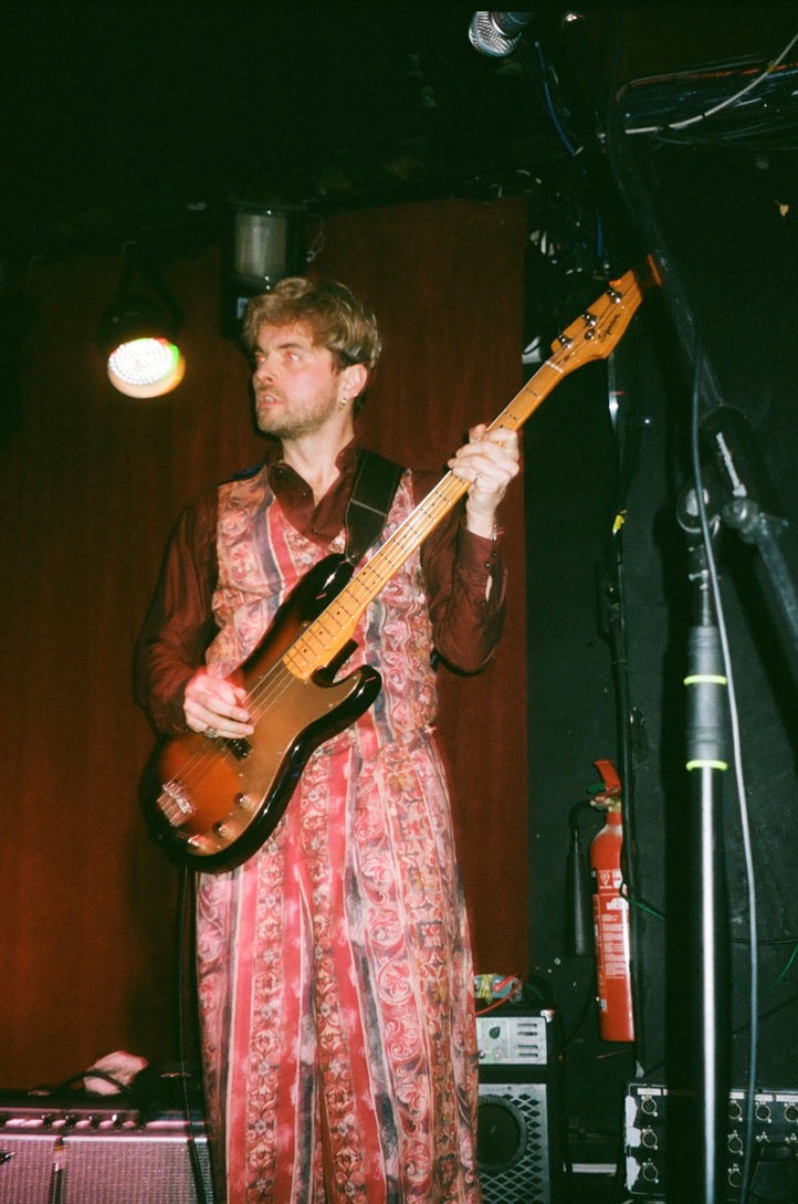 Person playing bass guitar on stage with musical equipment and lighting in the background