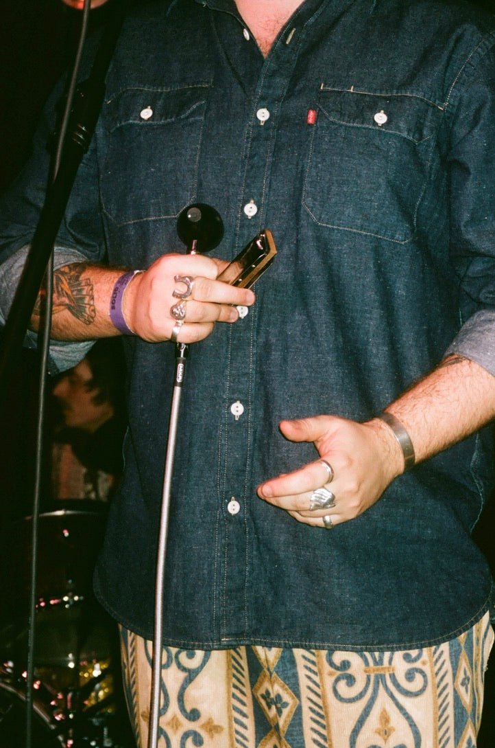 Person wearing a dark denim shirt with visible tattoos and jewelry, holding a smartphone.