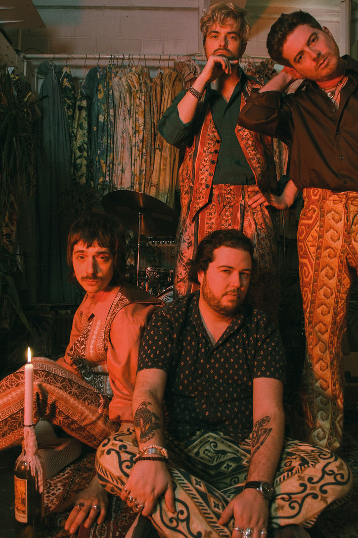 Four men in patterned clothing posing in a room with decorative elements.