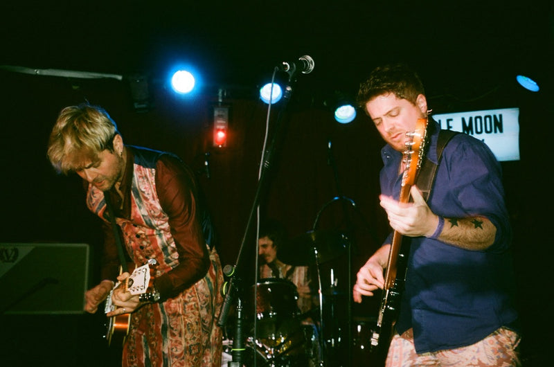 Two musicians playing guitar on stage with a microphone and lighting equipment.