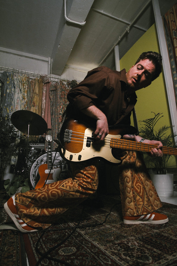 Person playing a bass guitar in a room with musical instruments and decor.
