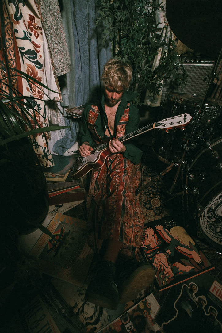 Person playing guitar in a room with patterned rug and plants