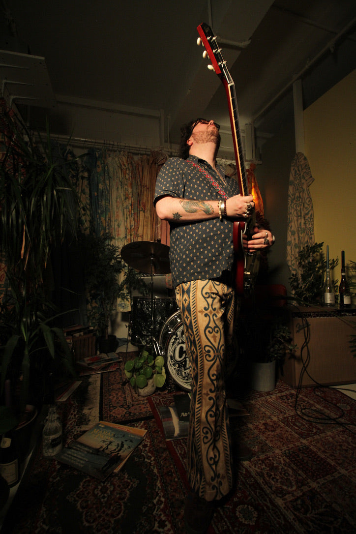 Man holding a guitar in a dimly lit room with musical equipment and decor.
