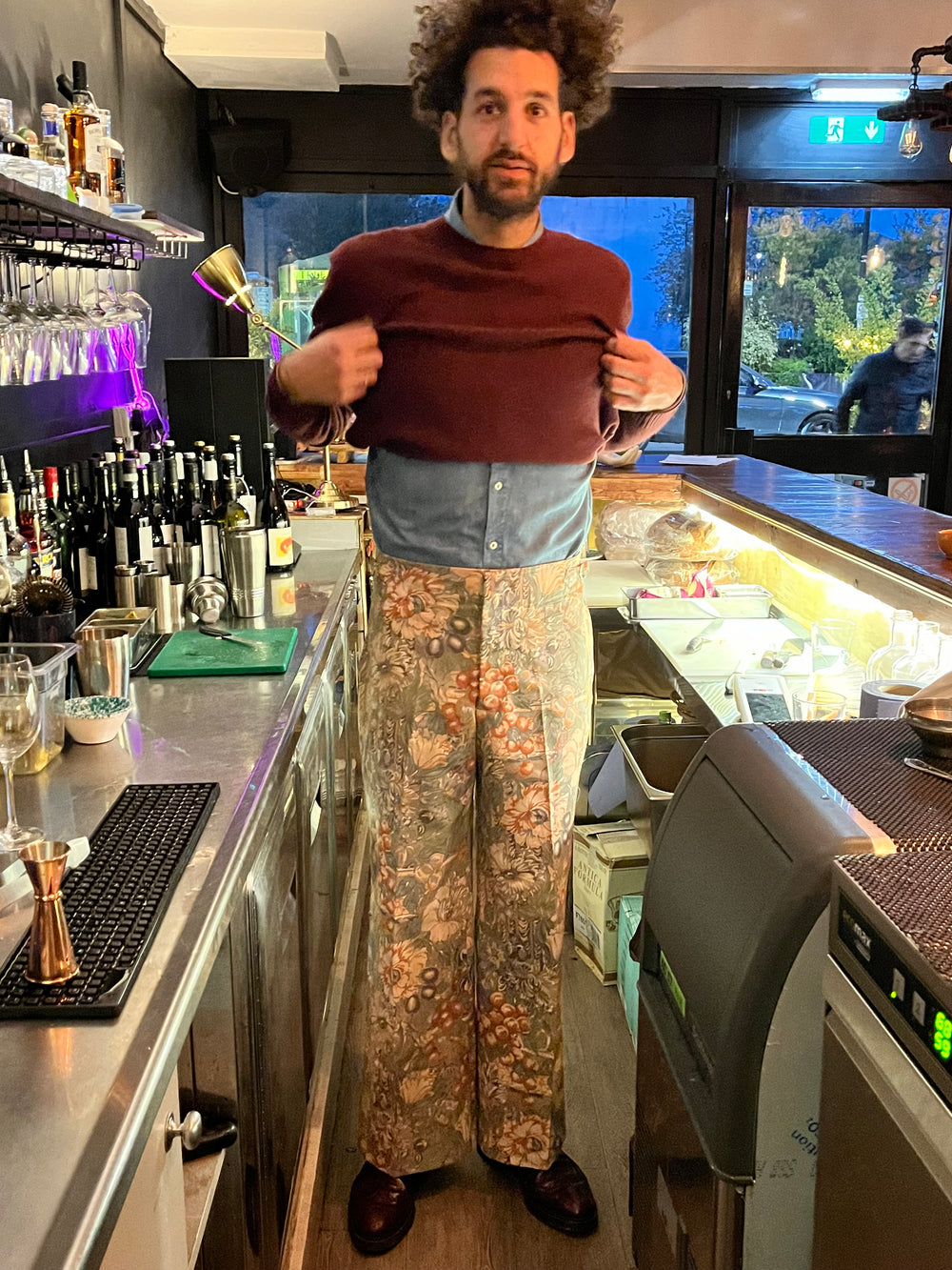 Person standing behind a counter with various items on it, including a computer screen displaying an image of a person.