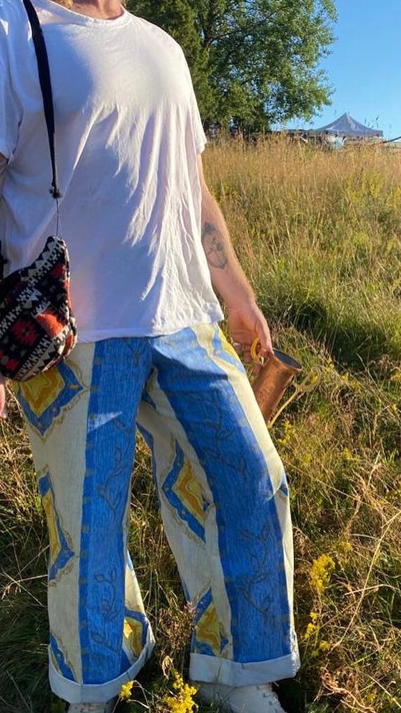 Person wearing a white shirt and blue patterned pants standing in a grassy field.