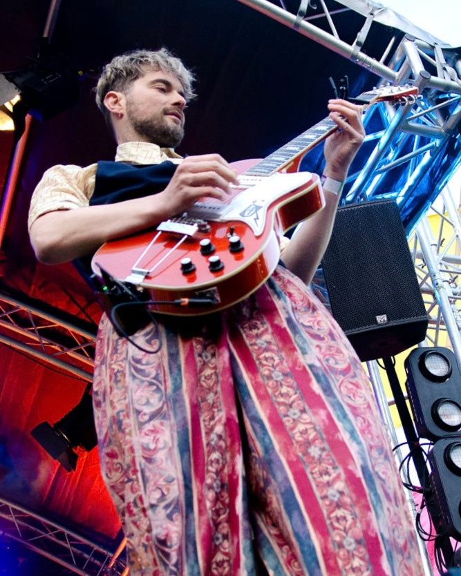 Person playing a red electric guitar on stage with musical equipment around
