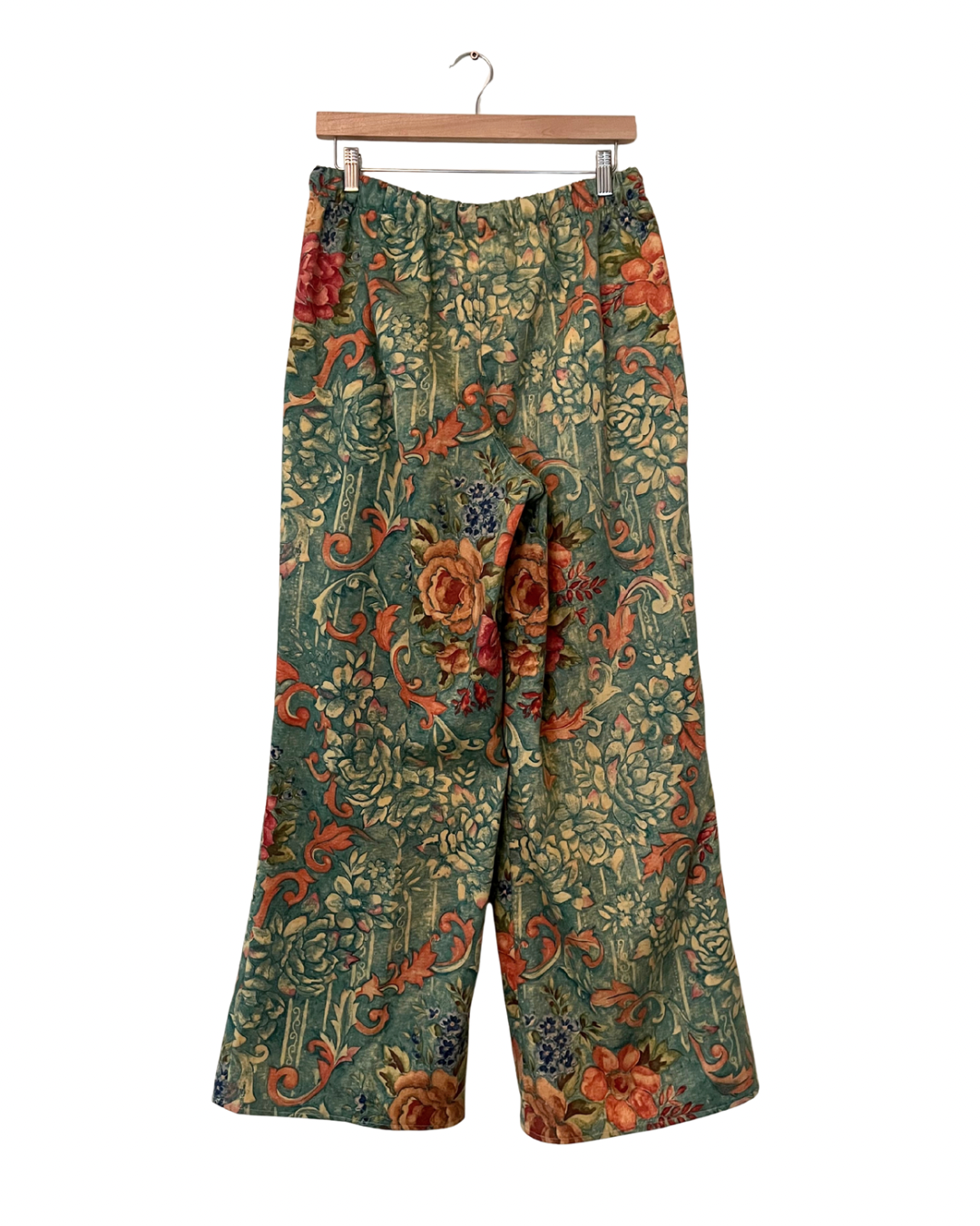Floral-patterned pants on a wooden hanger against a white background