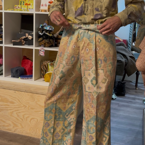 Person holding patterned pants in a room with shelves and furniture.