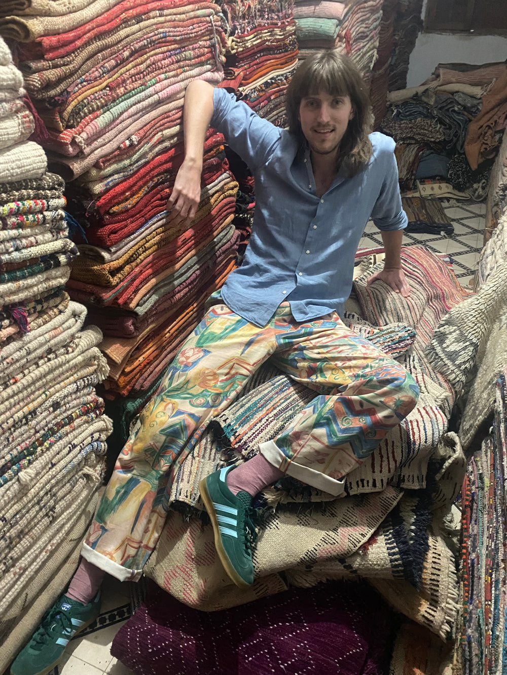 Person standing among various colorful rugs on a textured floor.