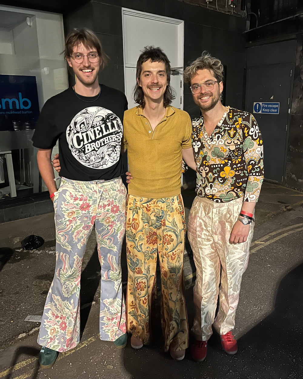Three people wearing patterned outfits standing together in an indoor setting.