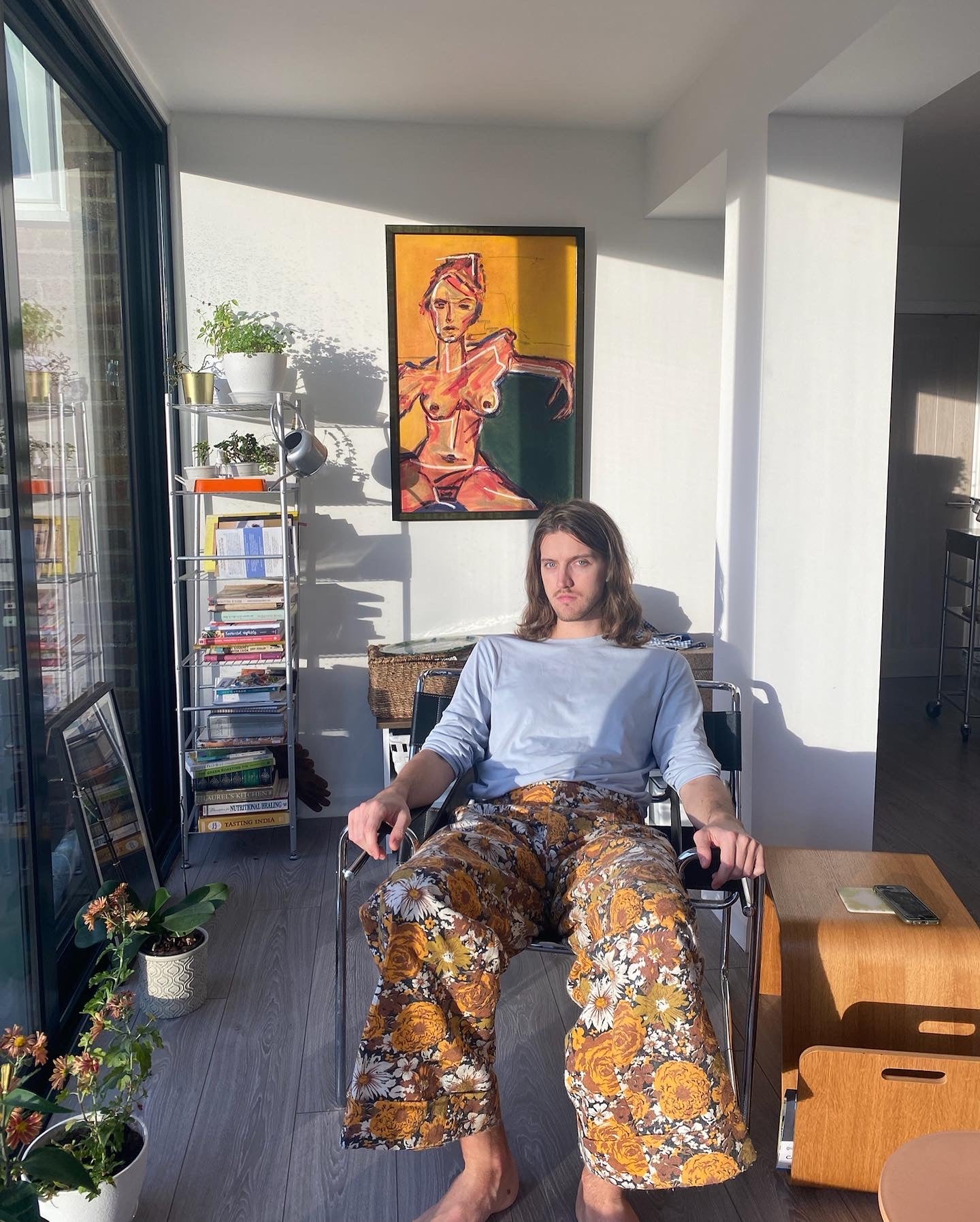 Person sitting in a chair with a colorful patterned garment, in a room with a painting on the wall.