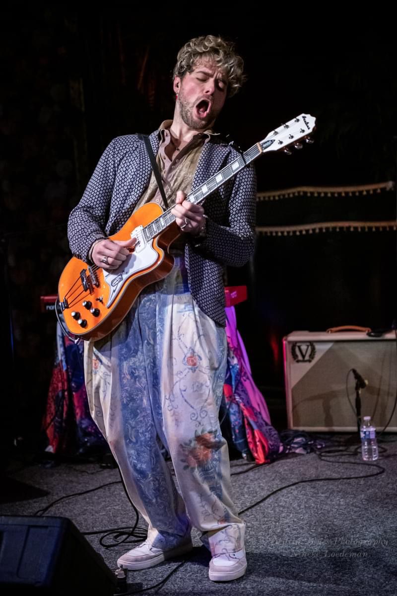 Person playing an electric guitar on stage with musical equipment in the background