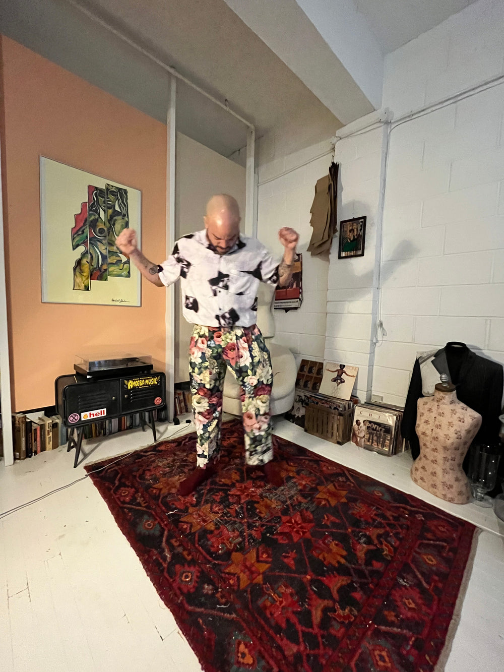 Person standing in a room with a painting on a table, a rug on the floor, and various items around.