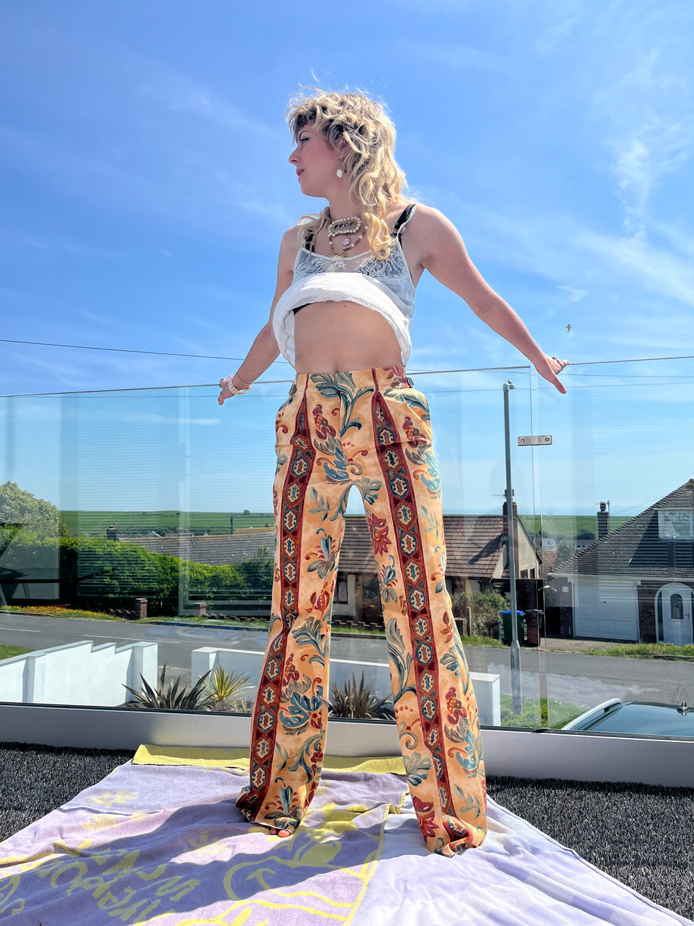 Person wearing a white top and patterned pants standing outdoors with a clear blue sky.