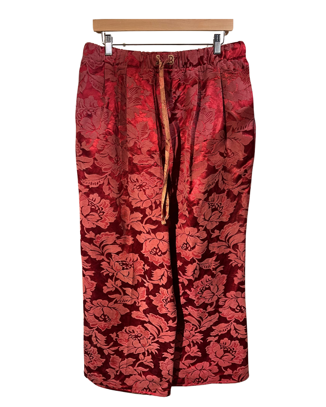 Red floral patterned pants on a hanger against a white background