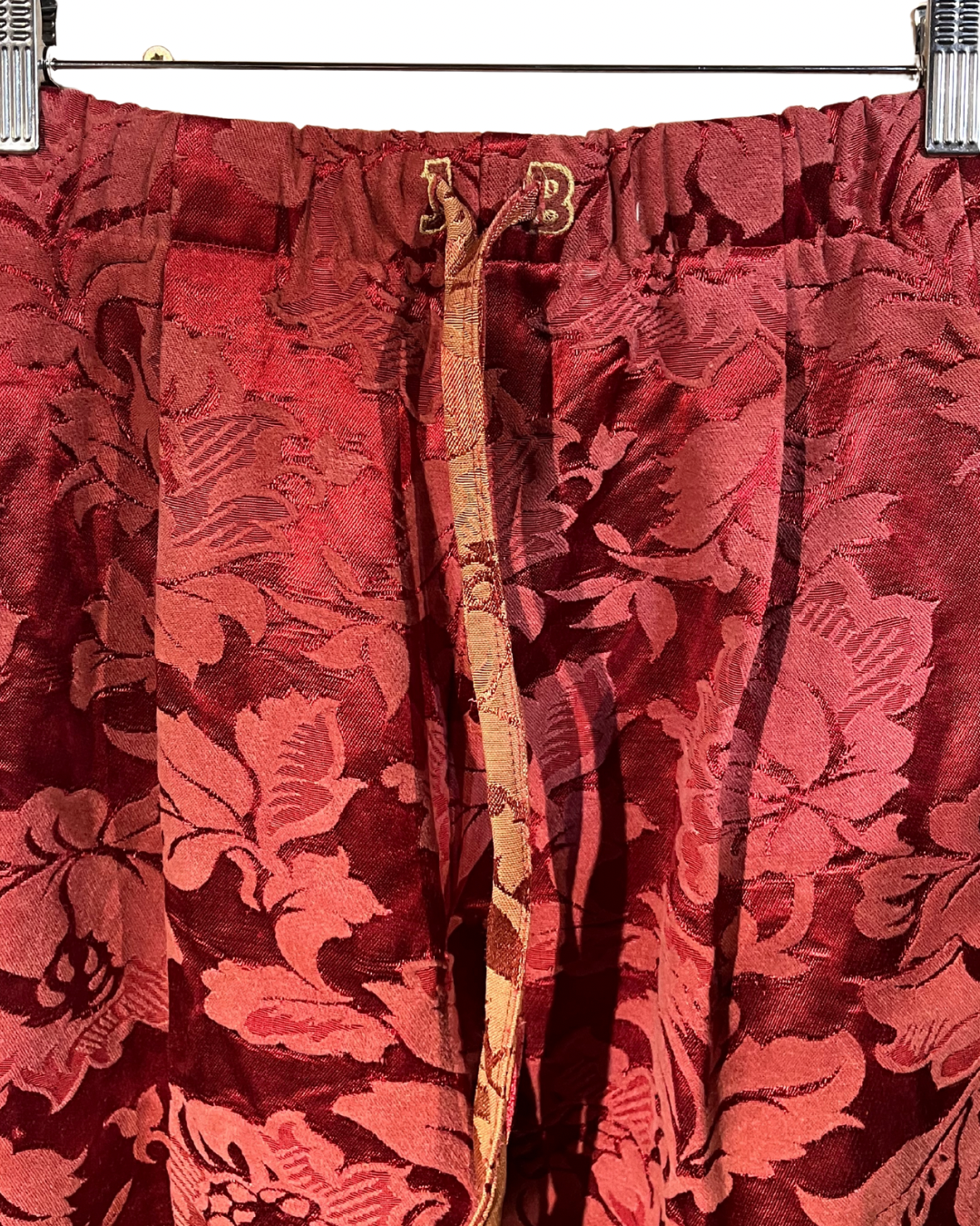 Red floral-patterned pants with a gold zipper on a hanger.