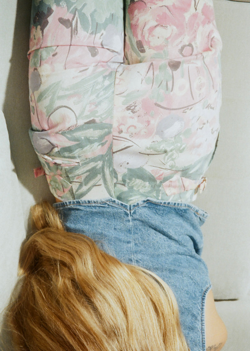 Person wearing a floral-patterned shirt and denim shorts with a neutral background