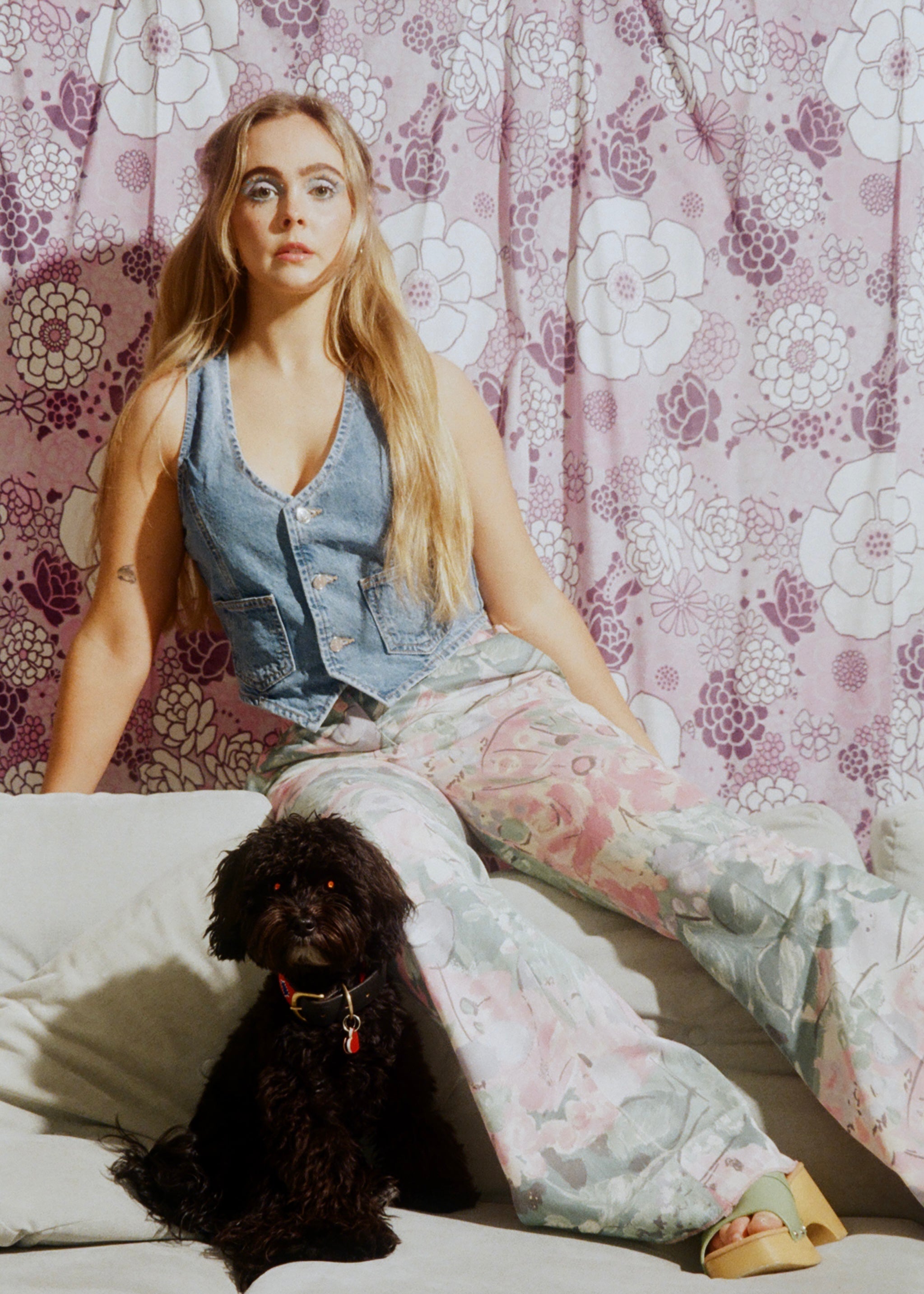 Woman sitting on a couch with a dog, floral patterned wall in the background