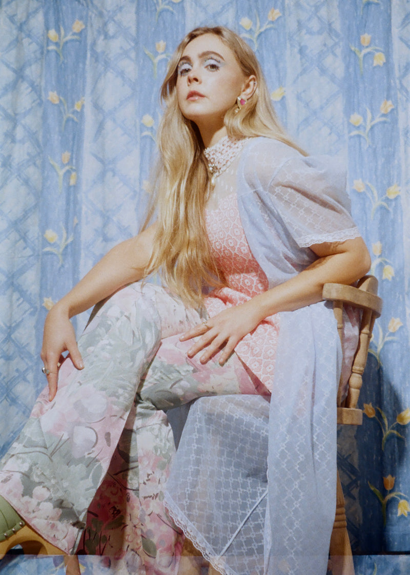 Woman in a floral dress sitting on a chair against a patterned blue background