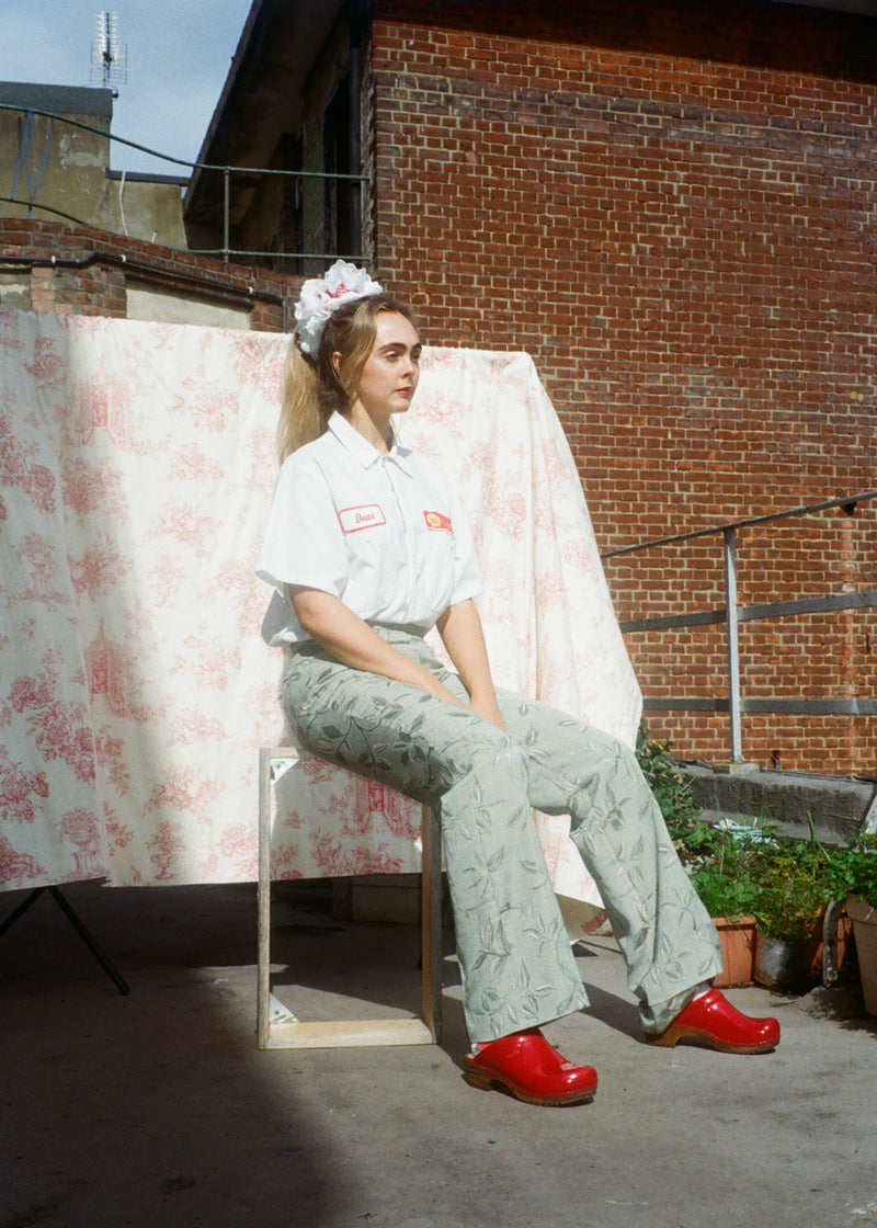 Person sitting on a chair with a floral curtain and brick wall in the background
