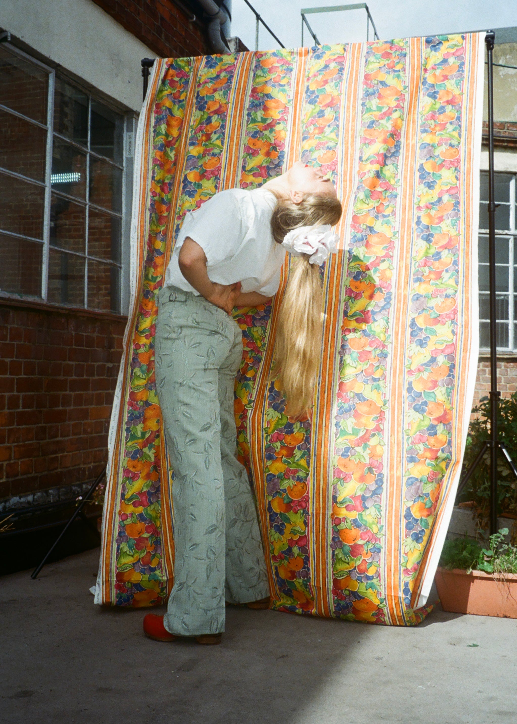 Person with long hair standing behind a colorful striped curtain outdoors.