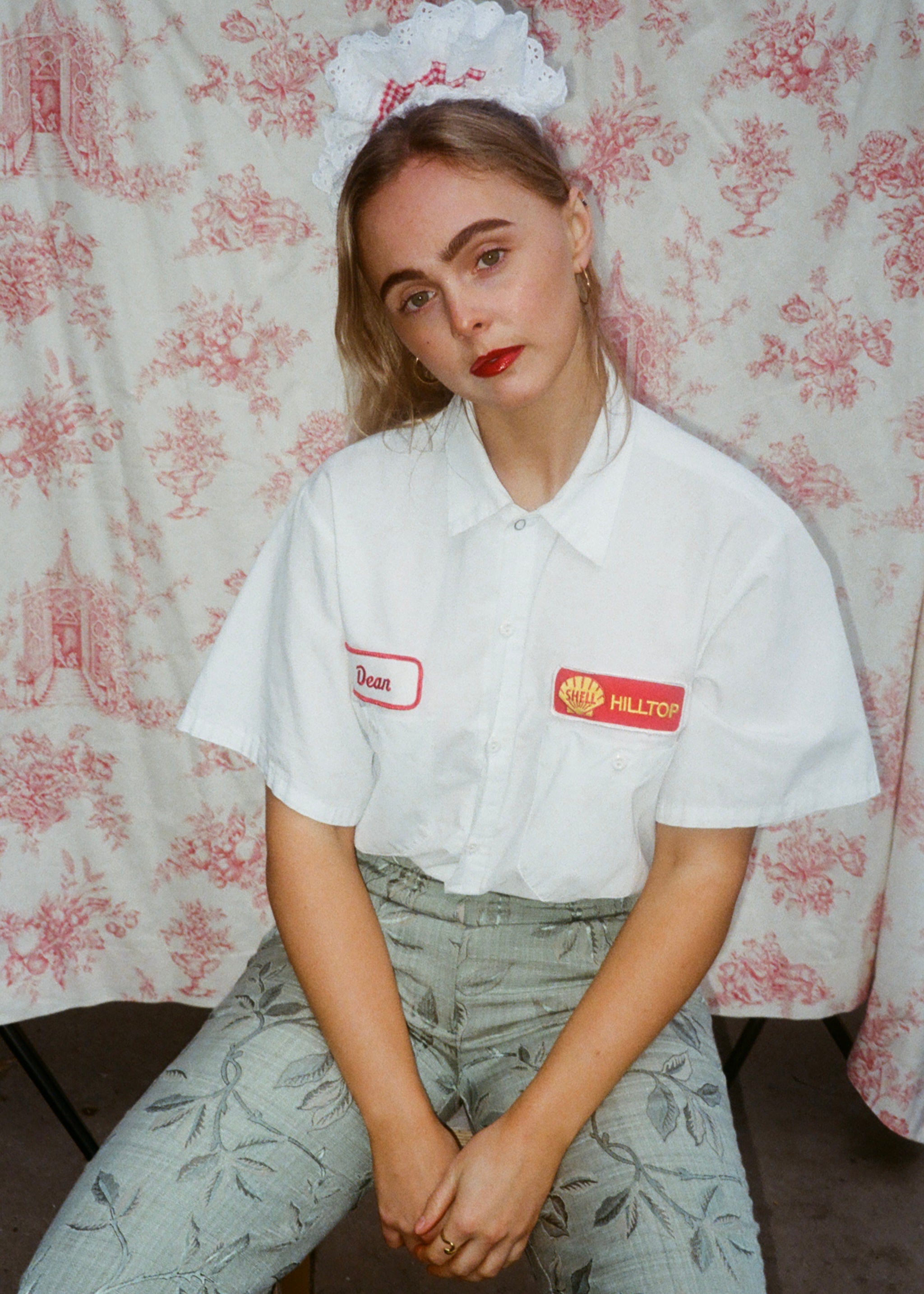 Person wearing a white shirt with logos in front of a floral patterned curtain