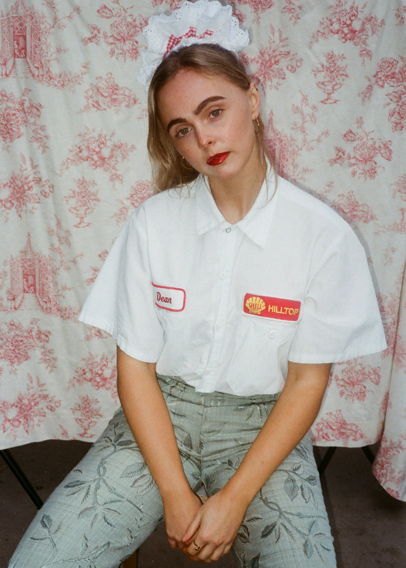 Person wearing a white shirt with logos in front of a floral patterned curtain