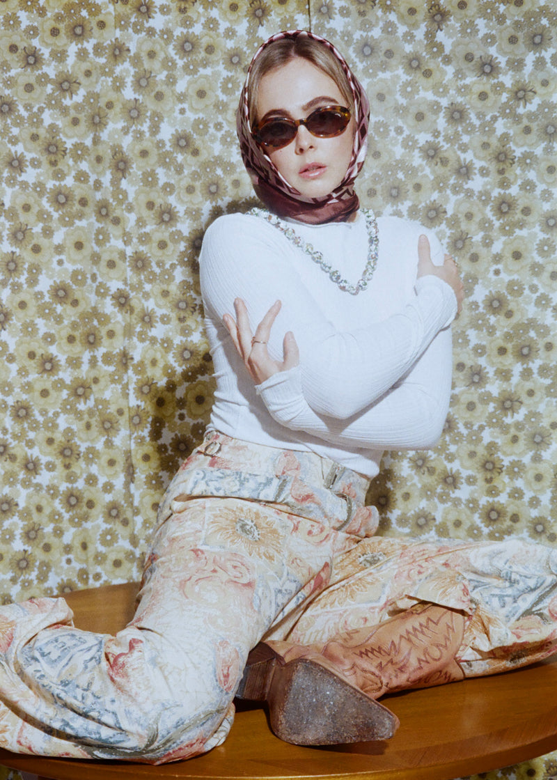 Person wearing sunglasses and a patterned outfit against a floral wallpaper background
