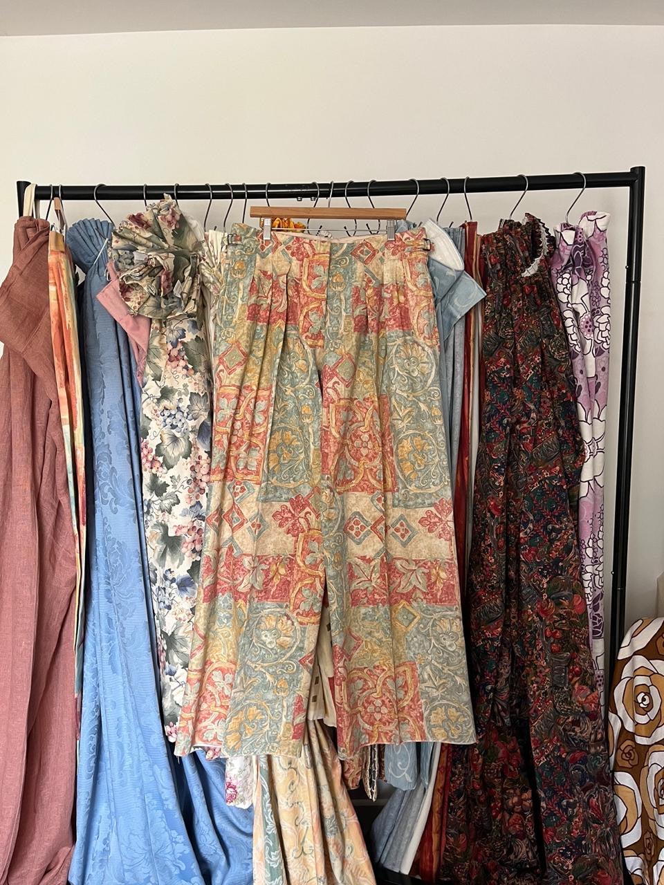 Colorful patterned pants hanging on a rack against a white wall.