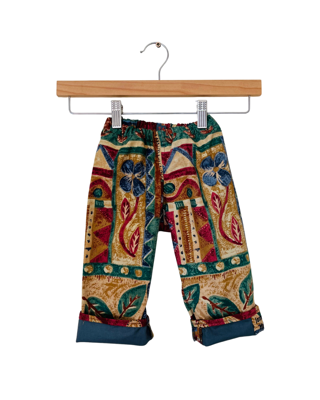 Colorful patterned pants on a wooden hanger against a white background