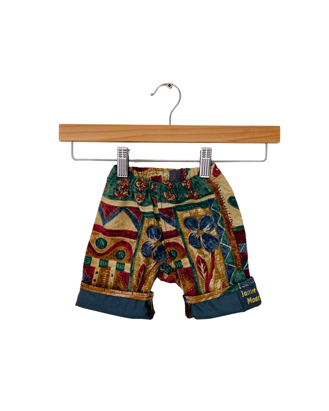 Colorful patterned trousers on a wooden hanger against a white background