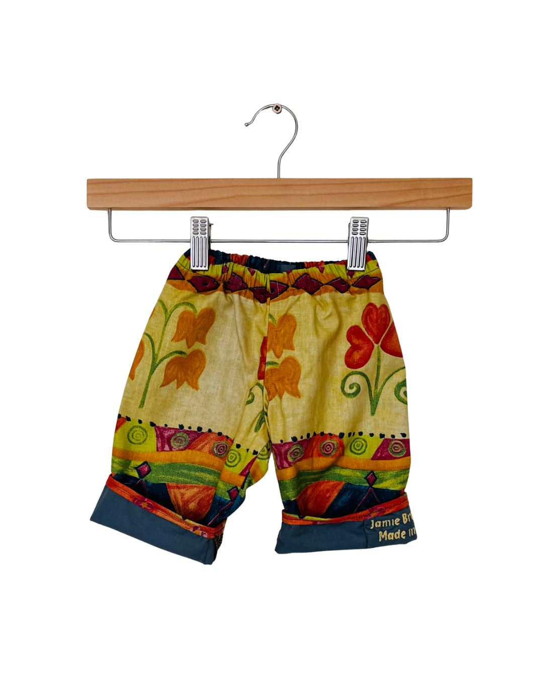 Colorful children's shorts with floral pattern on a wooden hanger against a white background