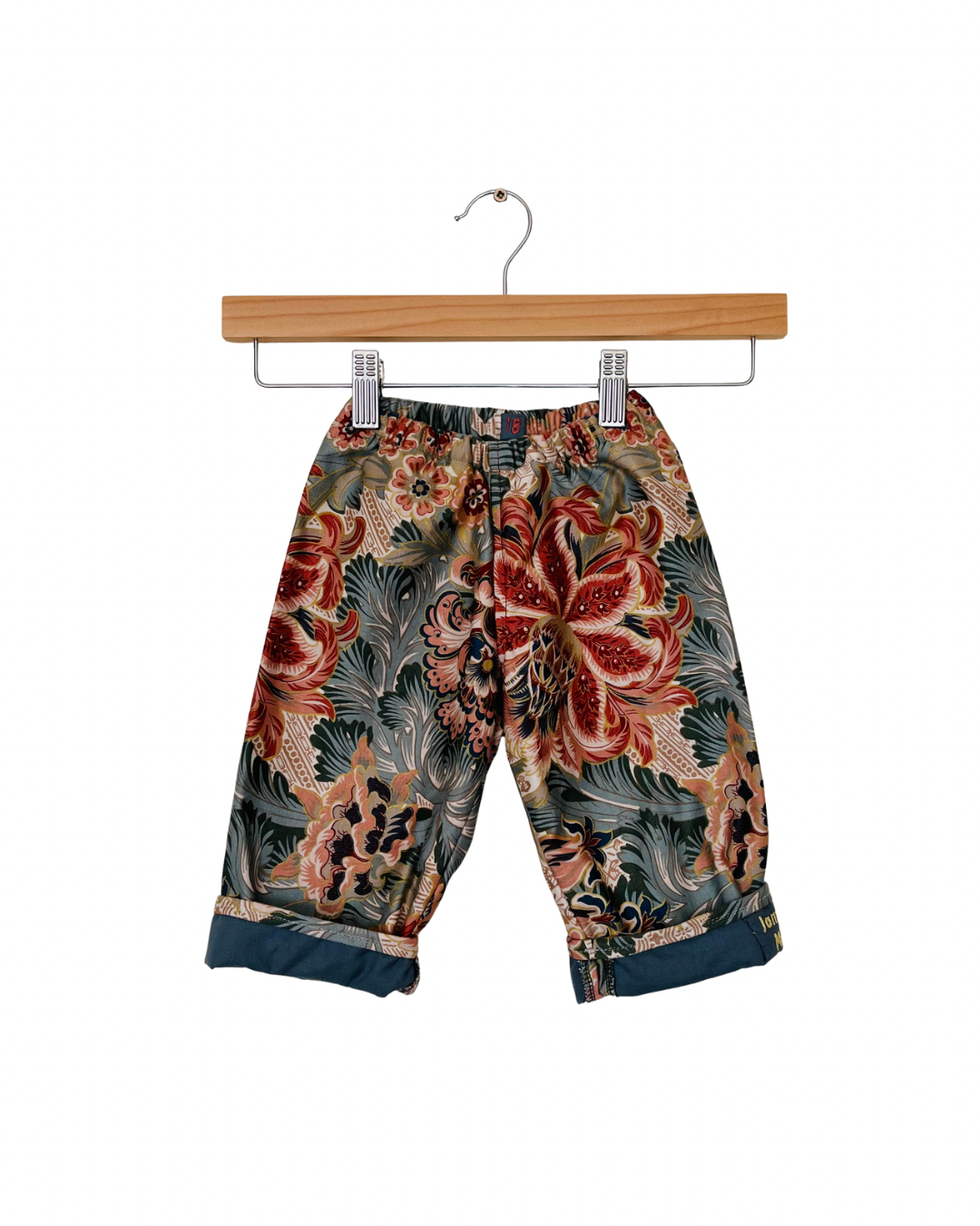 Floral-patterned pants on a wooden hanger against a white background