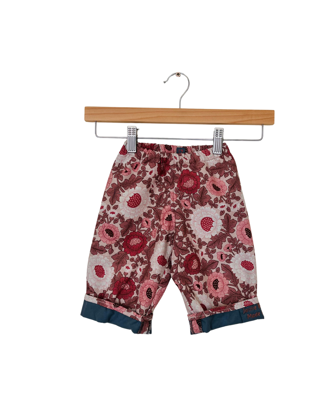 Floral-patterned pants on a wooden hanger against a white background