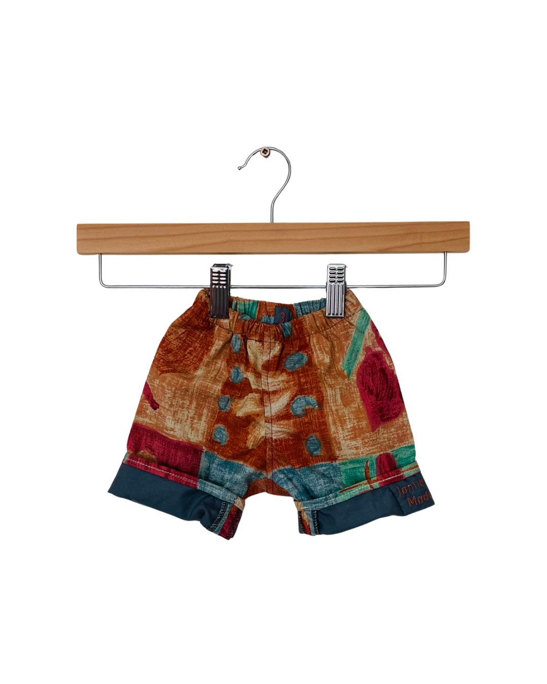 Colorful patchwork trousers on a wooden hanger against a white background