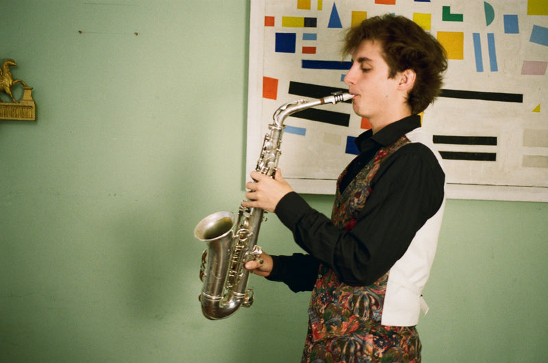 Person playing a saxophone in a room with a colorful abstract painting on the wall.