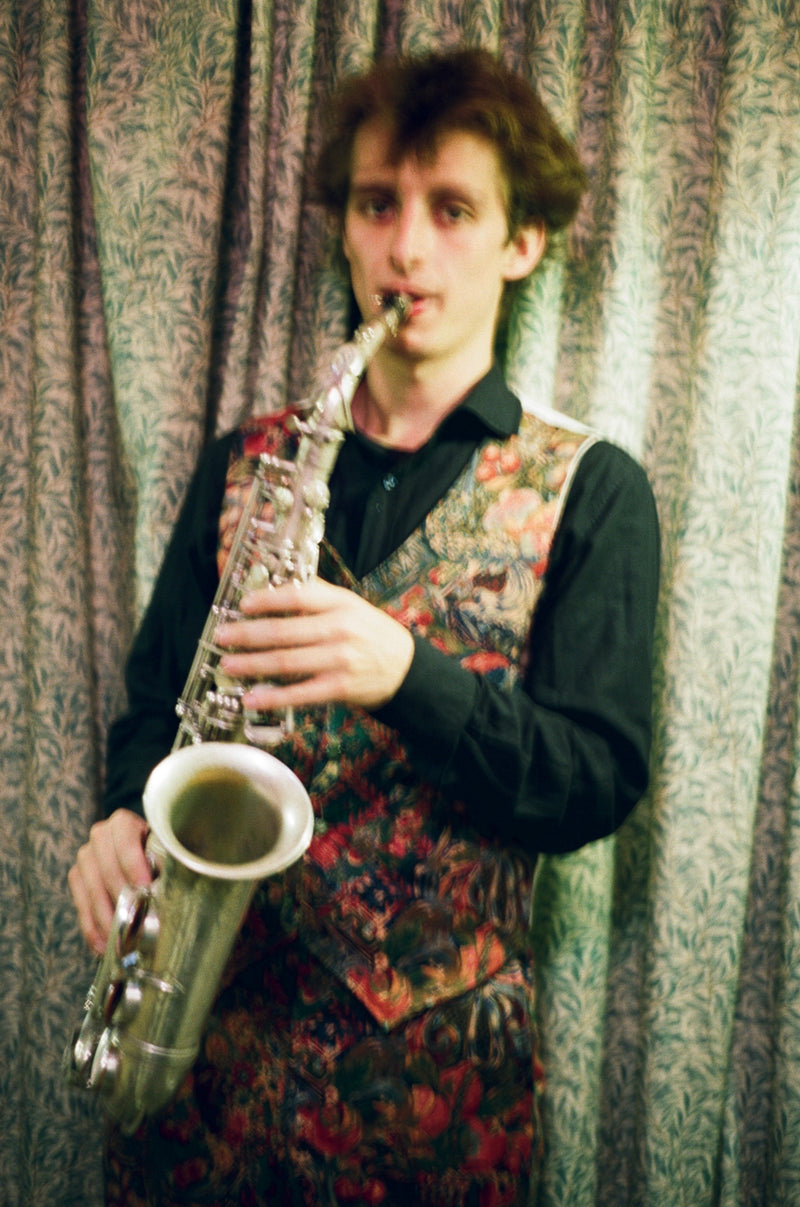 Person playing a saxophone against a patterned curtain