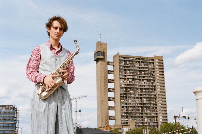 Person holding a saxophone with a cityscape background featuring tall buildings.