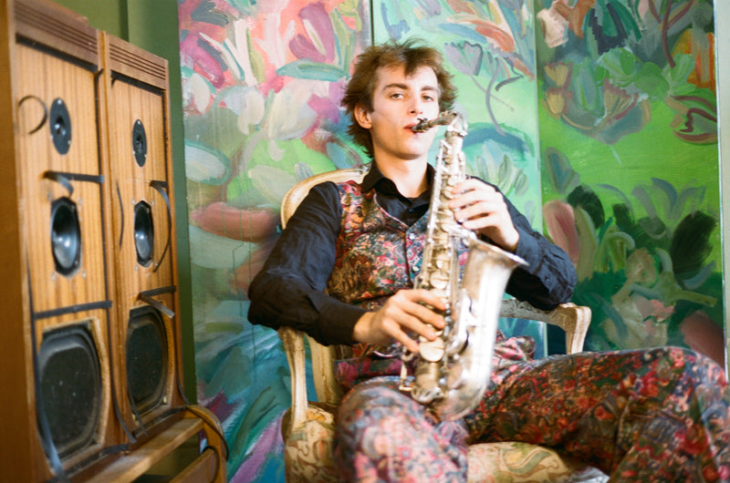 Person playing a saxophone in a colorful room with a large speaker cabinet.