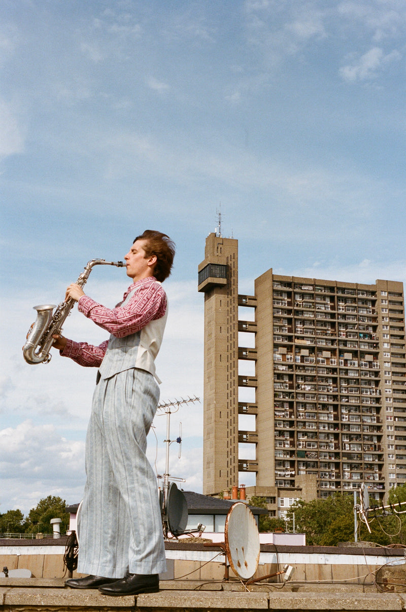 Person playing a saxophone on a rooftop with a high-rise building in the background
