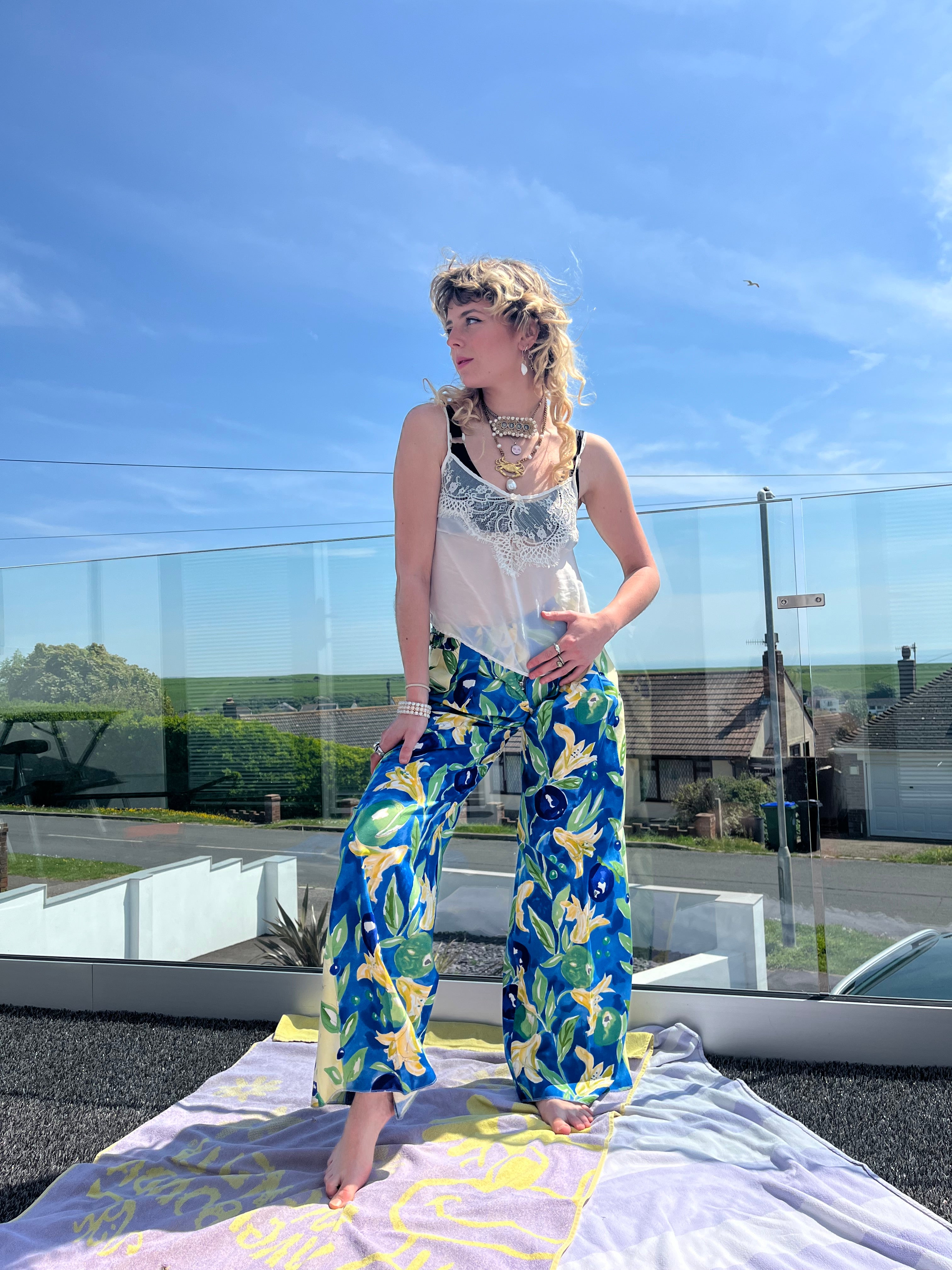 Person wearing a white top and colorful pants standing in front of a reflective surface.