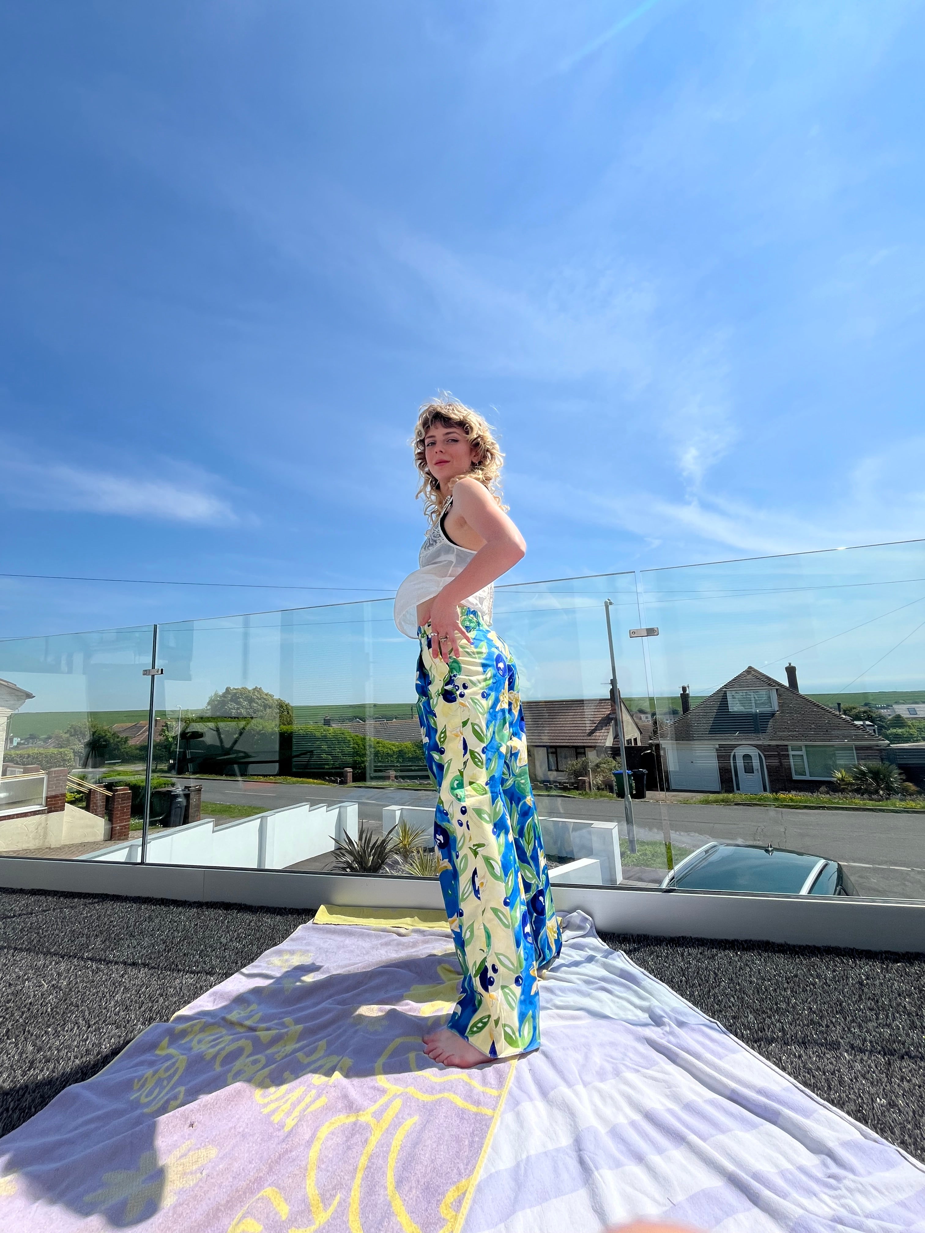 Woman holding a colorful trouser in front of a reflective surface with a clear blue sky.